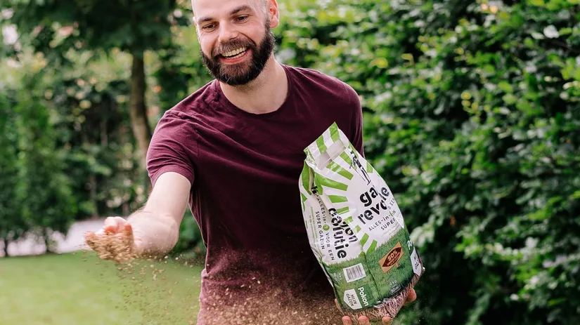 gazon bemesten.jpg Man strooit met een glimlach graszaad uit zijn hand terwijl hij een open zak vasthoudt in een groene tuin, licht naar voren gebogen en in beweging.
Tekst op de zak: "gazon revolutie", "ALLES‑IN‑1", "SUPER GAZON", "50%", "4 kg", "80 m²".