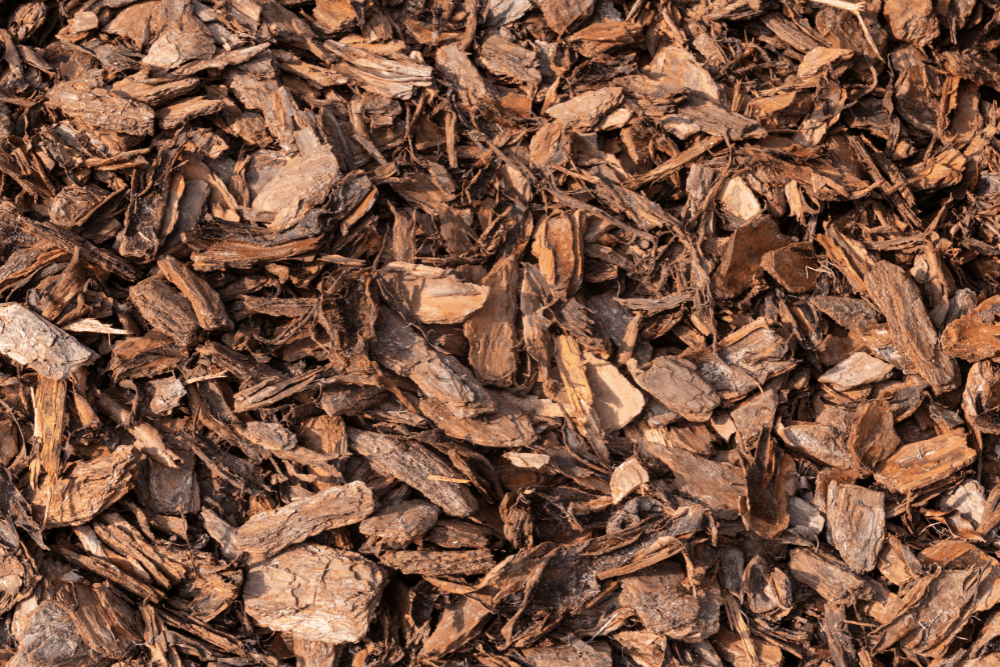 Houtsnippers bedekken de grond, los en door elkaar liggend, als bruin mulchmateriaal gebruikt in een tuin- of landschapsomgeving.
